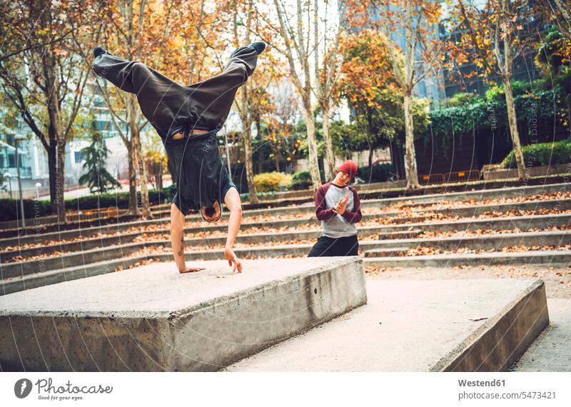 Young man performing handstand by friend in park autumn fall season seasons casual clothing casual wear leisure wear casual clothes Casual Attire color image
