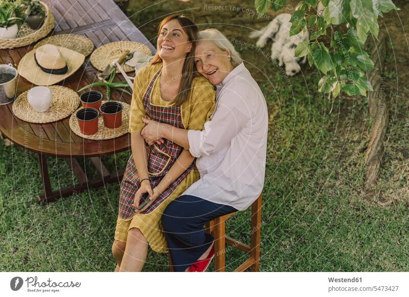 Happy mother embracing daughter while sitting by table in yard color image colour image Spain leisure activity leisure activities free time leisure time