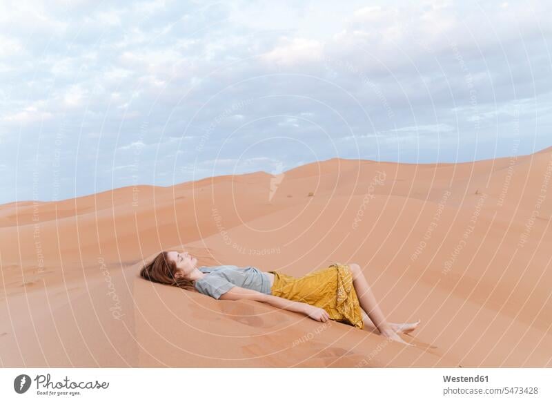 Young woman lying in sand dune in Sahara Desert, Merzouga, Morocco in the evening Late Evening solitary laying down lie lying down experience Experiences