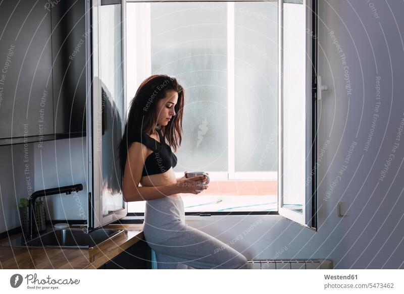 Serious beautiful young woman with cup of coffee at the window at home Coffee females women Coffee Cup Coffee Cups serious earnest Seriousness austere windows