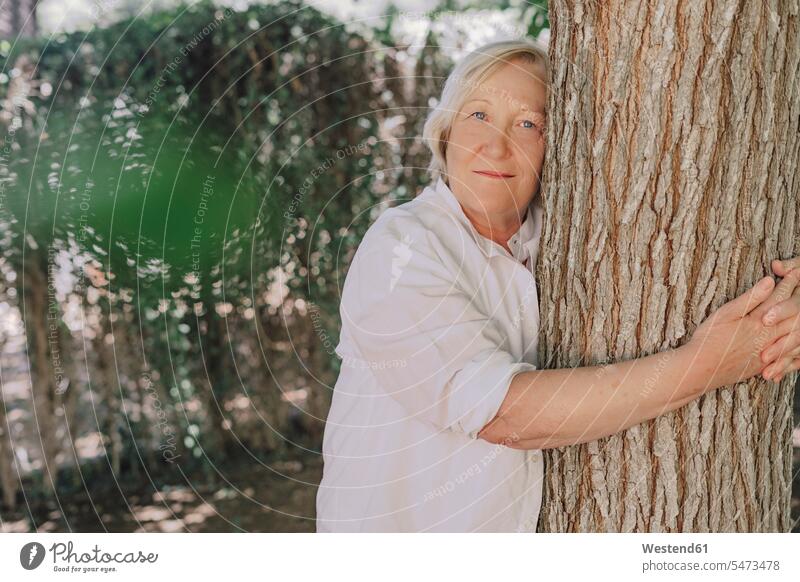 Senior woman embracing tree trunk while standing in yard color image colour image Spain leisure activity leisure activities free time leisure time