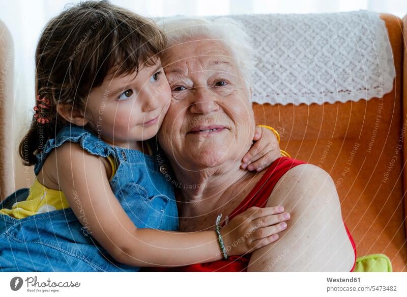 Smiling grandmother hugging her granddaughter at home chairs Arm Chair Arm Chairs armchairs touch relax relaxing cuddle snuggle snuggling smile Seated sit