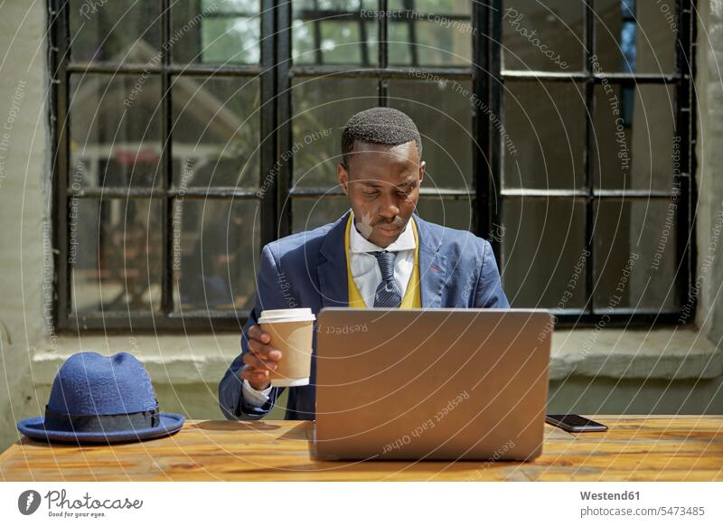 Stylish young businessman wearing old-fashioned suit using laptop at an outdoor cafe business life business world business person businesspeople Business man