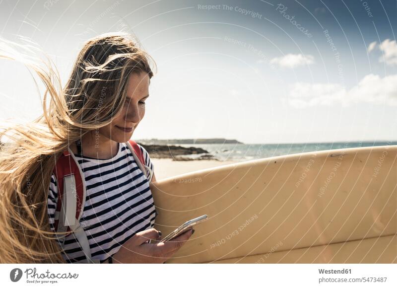 Young woman on the beach, carrying surfboard, using smartphone young women young woman beaches surfer female surfer surfers female surfers use surfboards