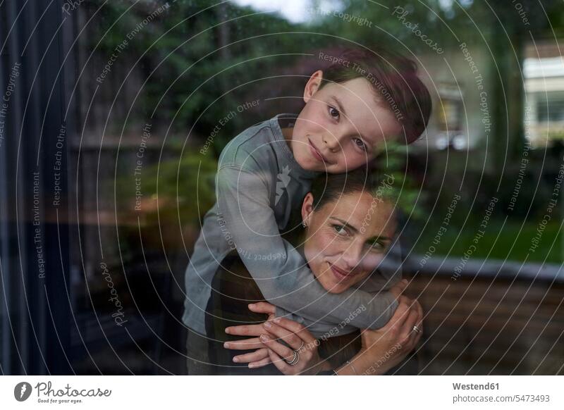 Loving son embracing mother while standing at home seen through window color image colour image Germany leisure activity leisure activities free time