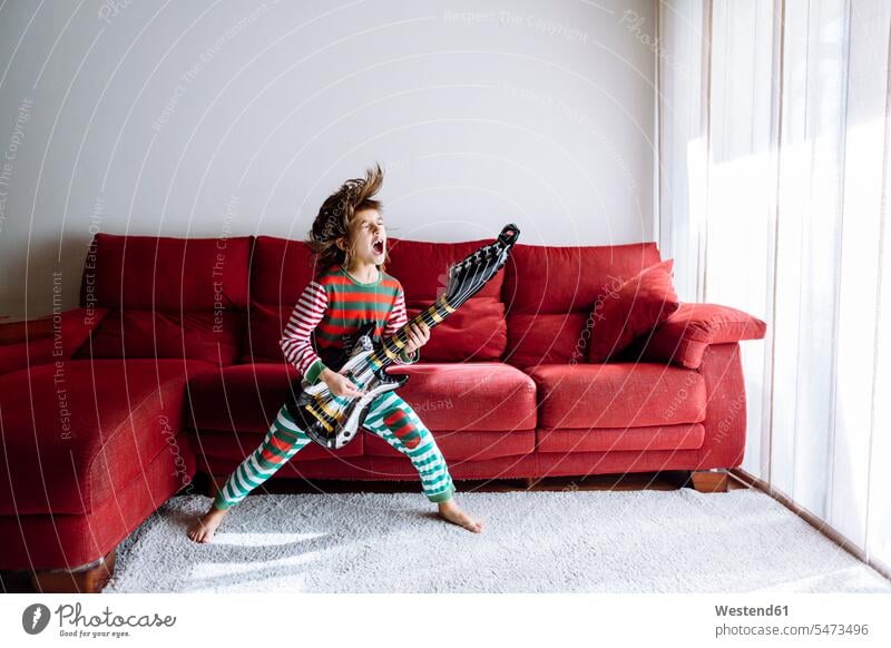 Happy girl playing guitar against sofa in living room color image colour image indoors indoor shot indoor shots interior interior view Interiors day
