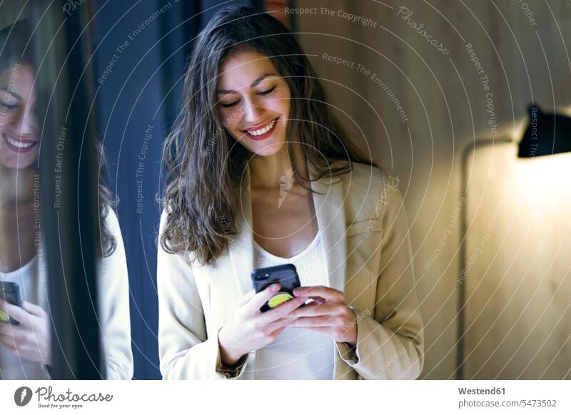 Smiling young businesswoman checking cell phone at the window human human being human beings humans person persons caucasian appearance caucasian ethnicity