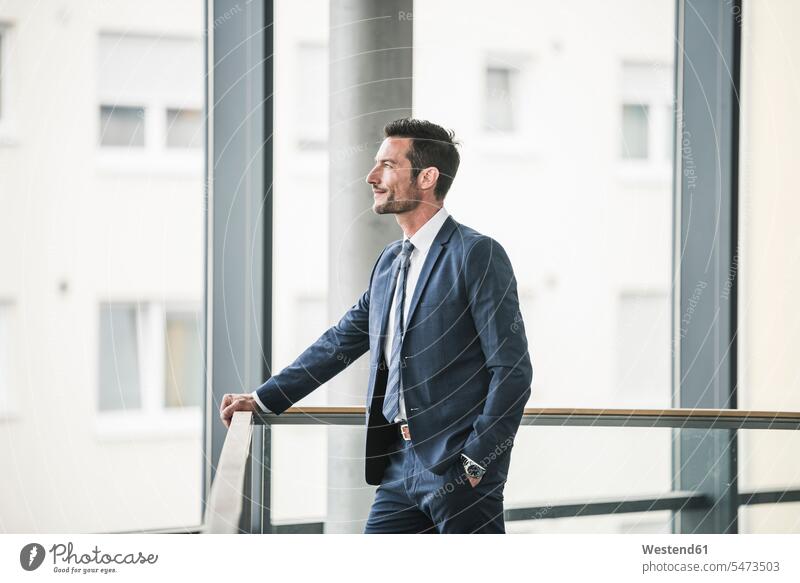 Successful businessman standing in office building, looking out of window, daydreaming offices office room office rooms thinking Vision Visions Businessman