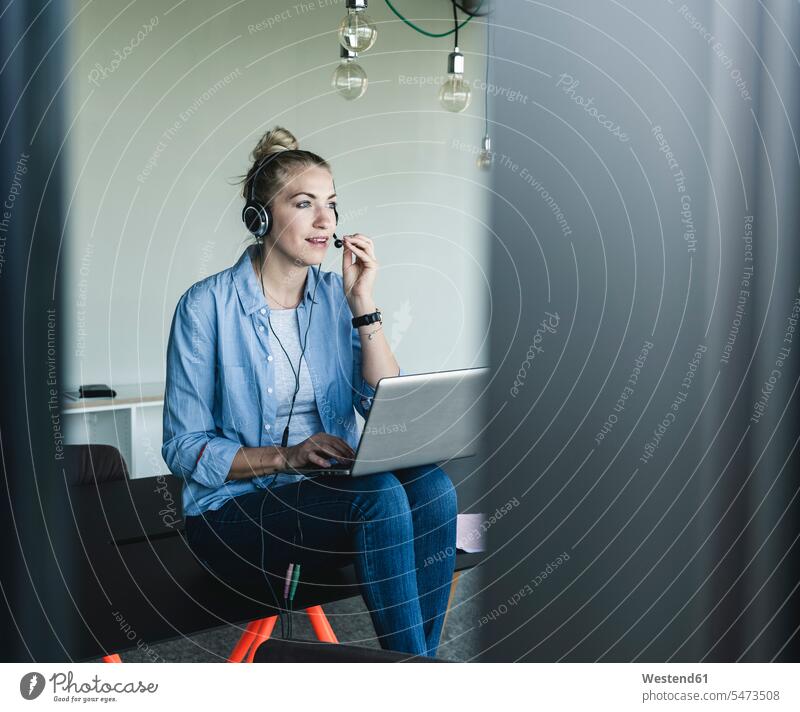 Young businesswoman sitting at desk, making a call, using headset and laptop telephone call Phone Call Laptop Computers laptops notebook on the phone