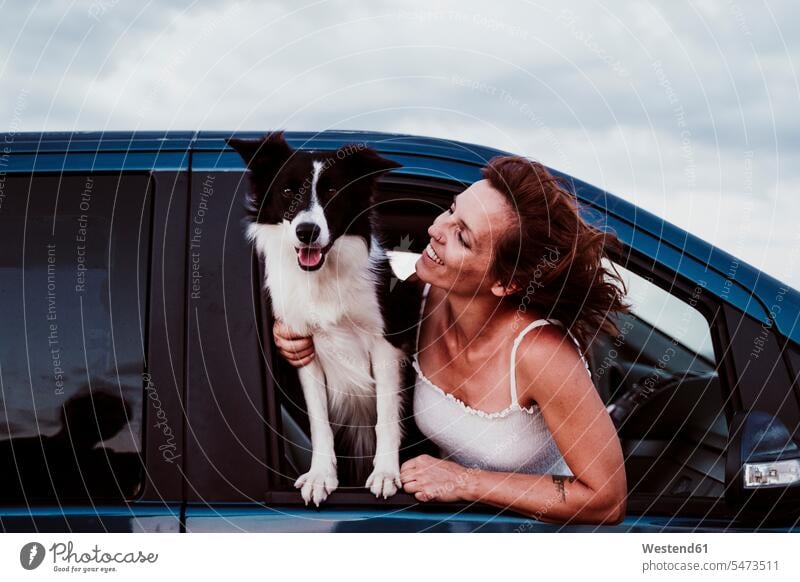 Smiling woman looking at dog while leaning through car window color image colour image Spain leisure activity leisure activities free time leisure time dogs
