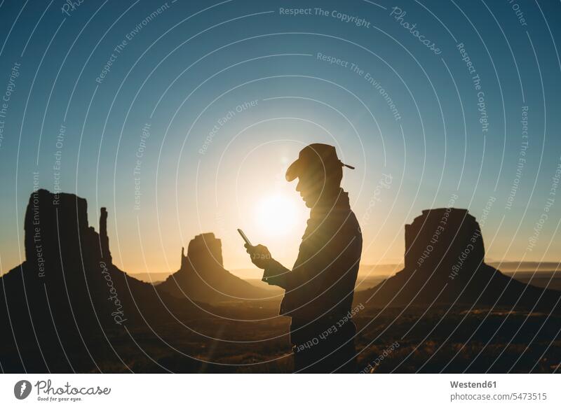 USA, Utah, Monument Valley, silhouette of man with cowboy hat looking at mobile phone at sunrise males cowboy hats eyeing Smartphone iPhone Smartphones sun rise