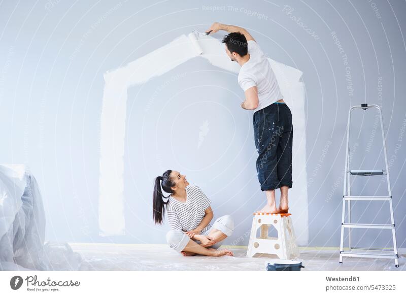 Couple painting house shape on wall in new apartment shapes flat flats apartments houses walls couple twosomes partnership couples people persons human being