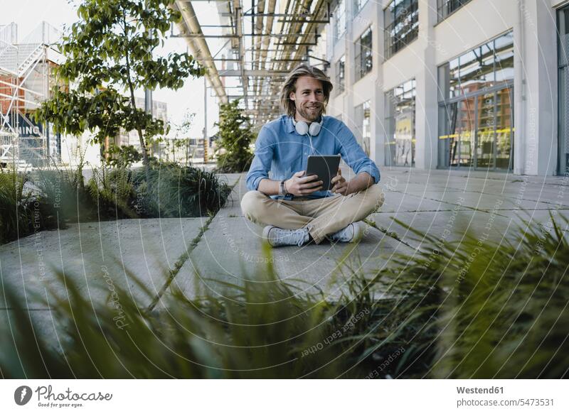 Smiling young man sitting on pavement using tablet human human being human beings humans person persons caucasian appearance caucasian ethnicity european 1