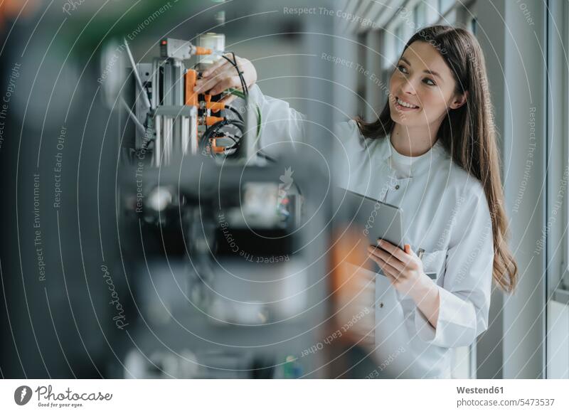 Smiling female scientist holding digital tablet inventing machinery in laboratory color image colour image indoors indoor shot indoor shots interior