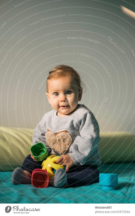 Portrait of baby girl sitting on bed playing with plastic toy Seated baby girls female toys portrait portraits infants nurselings babies beds people persons