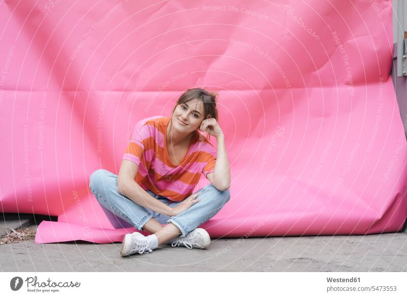 Confident young woman sitting on pink background carefree Seated happiness happy Pink background magenta females women coloured background colored background