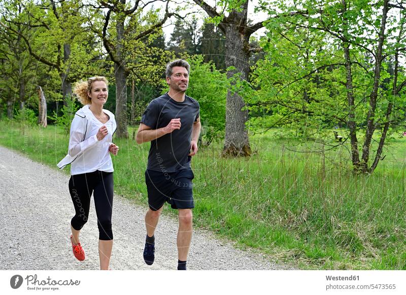 Couple running on dirt road against trees in forest color image colour image Germany wood woods forests nature natural world the natural world outdoors