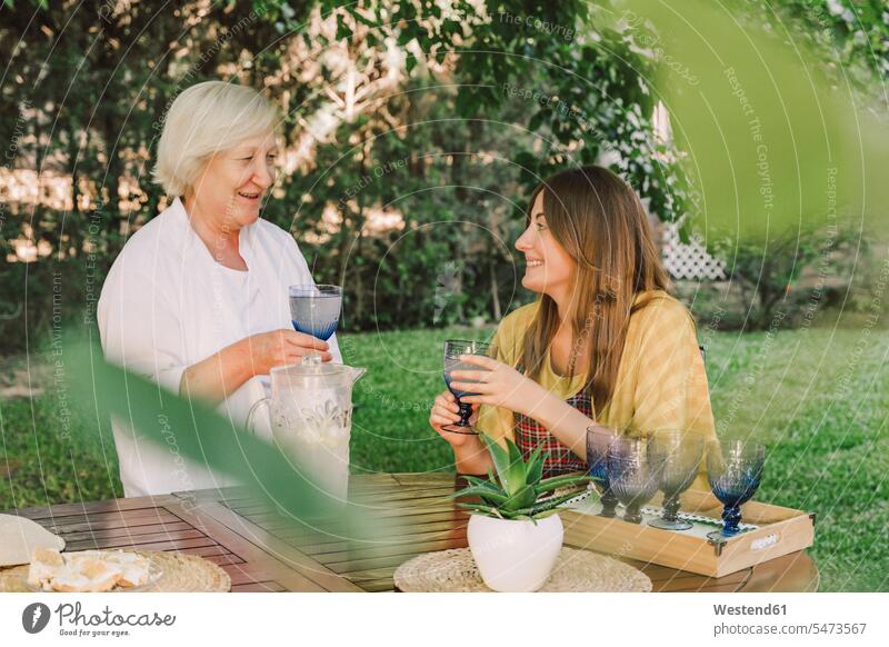 Smiling mother and daughter enjoying drinks while talking in yard color image colour image Spain leisure activity leisure activities free time leisure time