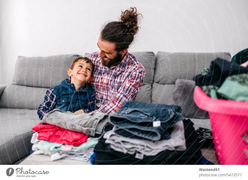 Father and son sitting together on the couch having fun while folding laundry father pa fathers daddy papa Fun funny Laundry sons manchild manchildren settee