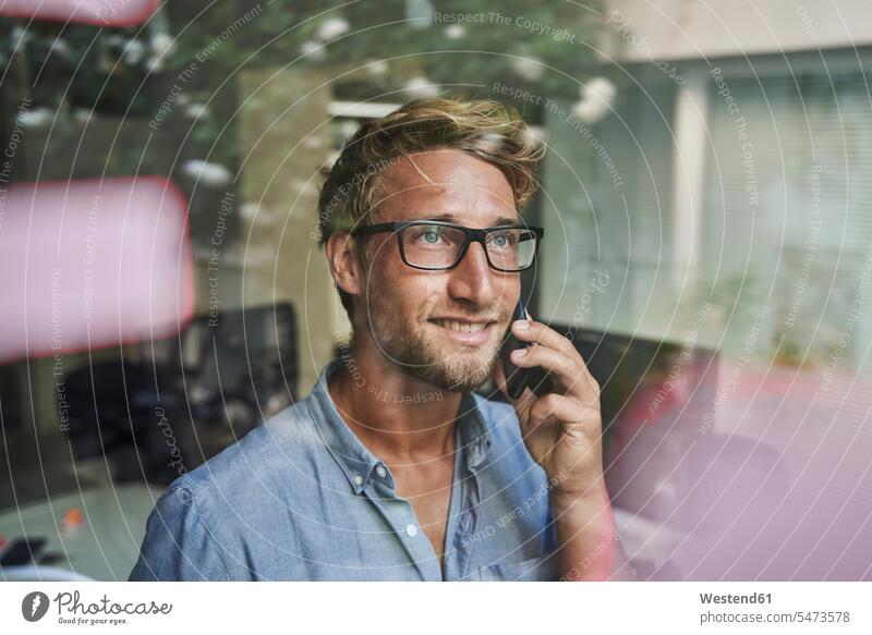Casual young businessman on the phone behind windowpane in office business life business world business person businesspeople Business man Business men