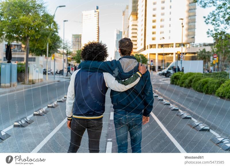 Rear view of two men embracing on the street in the city, Barcelona, Spain human human being human beings humans person persons caucasian appearance