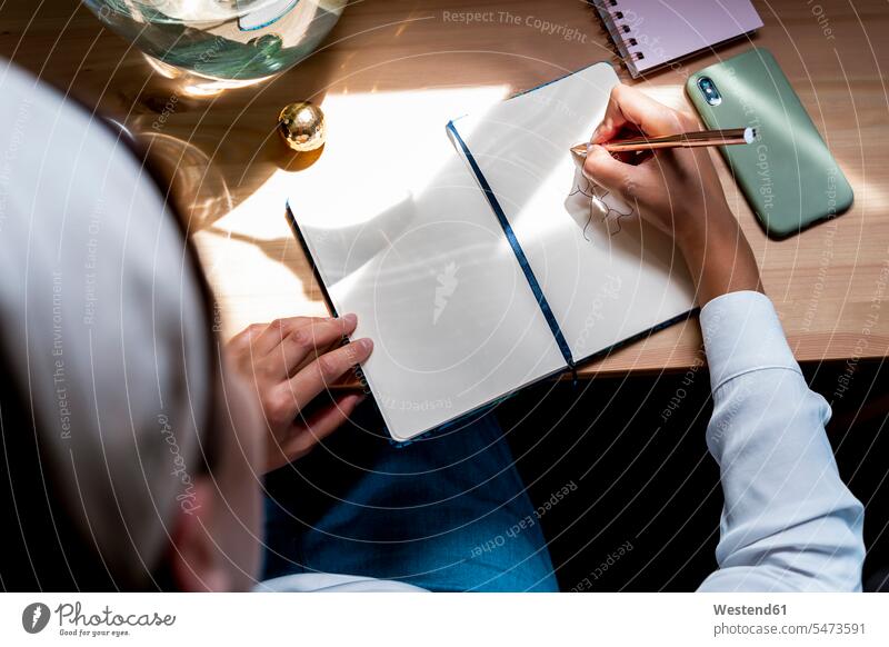 Mid adult woman drawing in diary on desk at home color image colour image Spain indoors indoor shot indoor shots interior interior view Interiors day
