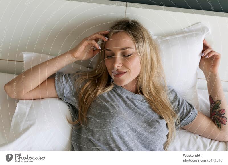 Smiling blond young woman lying in bed laying down lie lying down blond hair blonde hair females women smiling smile beds people persons human being humans