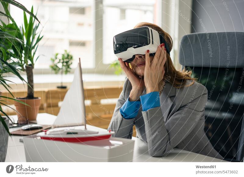 Businesswoman sitting at desk with a ship model, looking through VR glasses Virtual Reality Glasses Virtual-Reality Glasses virtual reality headset vr headset