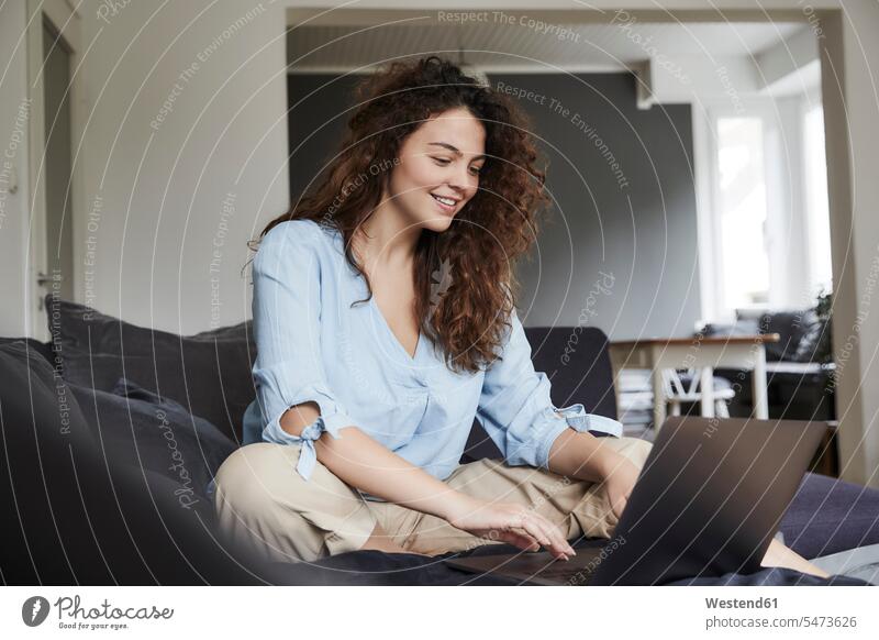 Young woman using laptop while sitting on sofa at home color image colour image indoors indoor shot indoor shots interior interior view Interiors day