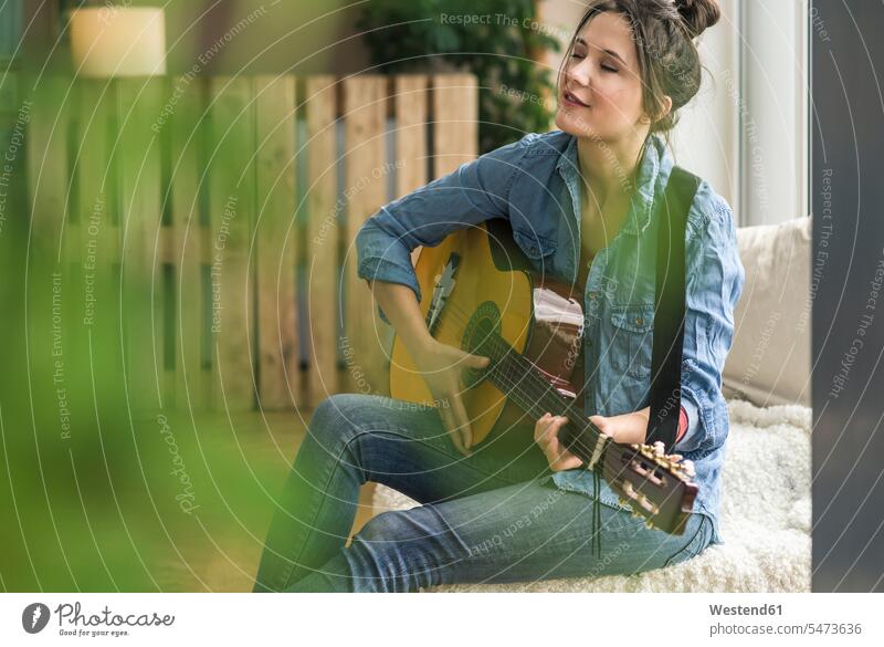 Passionate woman playing guitar at home sitting Seated females women guitars passionate Adults grown-ups grownups adult people persons human being humans