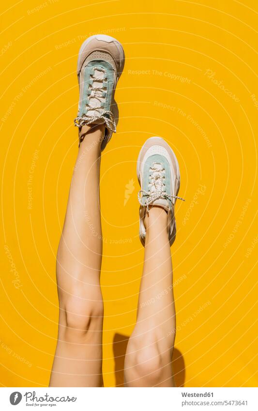 Woman's legs in sports shoes over yellow wall during sunny day color image colour image outdoors location shots outdoor shot outdoor shots daylight shot