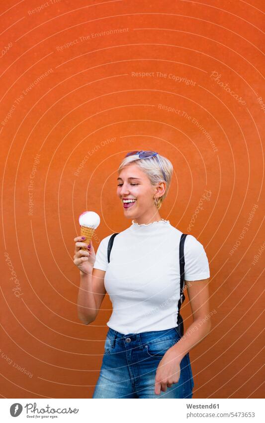 Laughing young woman with ice cream cone in front of orange background laughing Laughter Ice Cream Cone ice-cream cone Ice Cream Cones ice-cream wafer females