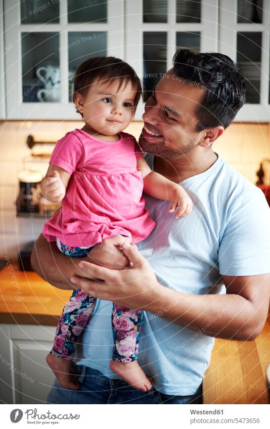 Smiling father holding baby girl in kitchen at home smiling smile daughter daughters pa fathers daddy dads papa infants nurselings babies child children family