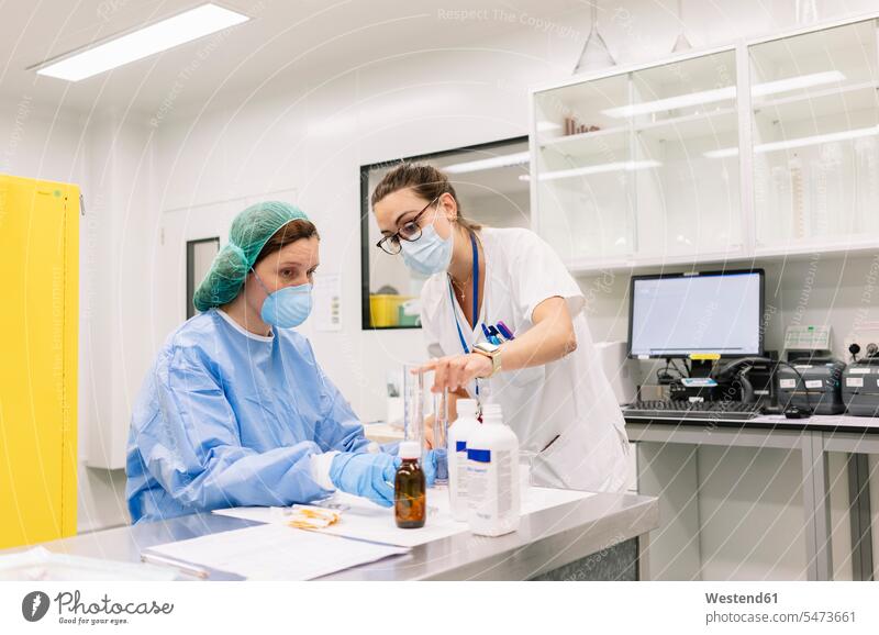 Female pharmacists discussing while making medicines in laboratory at hospital color image colour image Spain indoors indoor shot indoor shots interior