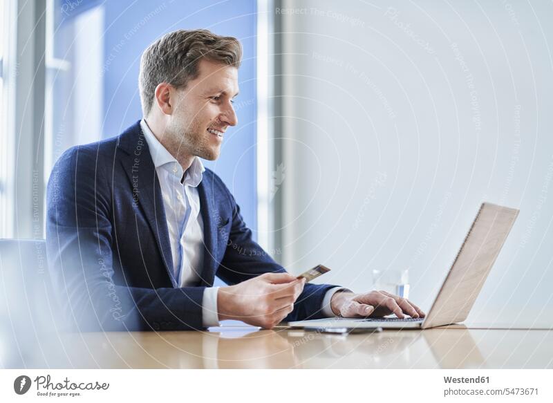 Businessman holding credit card and using laptop at desk in office Occupation Work job jobs profession professional occupation business life business world