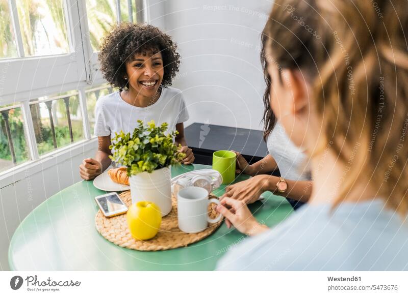 Three happy women sitting at table at home drinking coffee together Coffee happiness Seated Table Tables woman females female friends Drink beverages Drinks