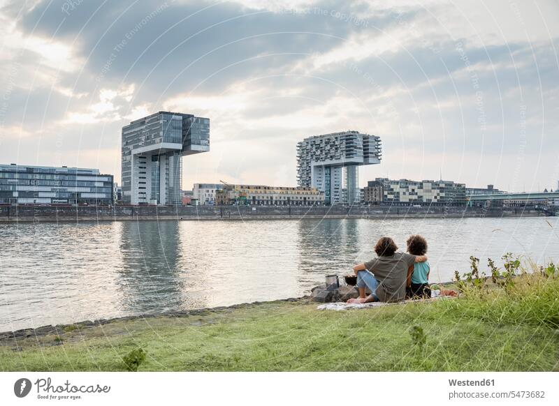 Germany, Cologne, couple relaxing at the riverside at sunset relaxed relaxation riverbank twosomes partnership couples sunsets sundown water's edge waterside