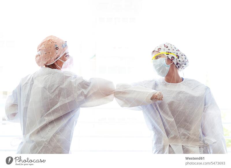 Doctor and assistant greeting with touching elbow while standing against window color image colour image indoors indoor shot indoor shots interior interior view