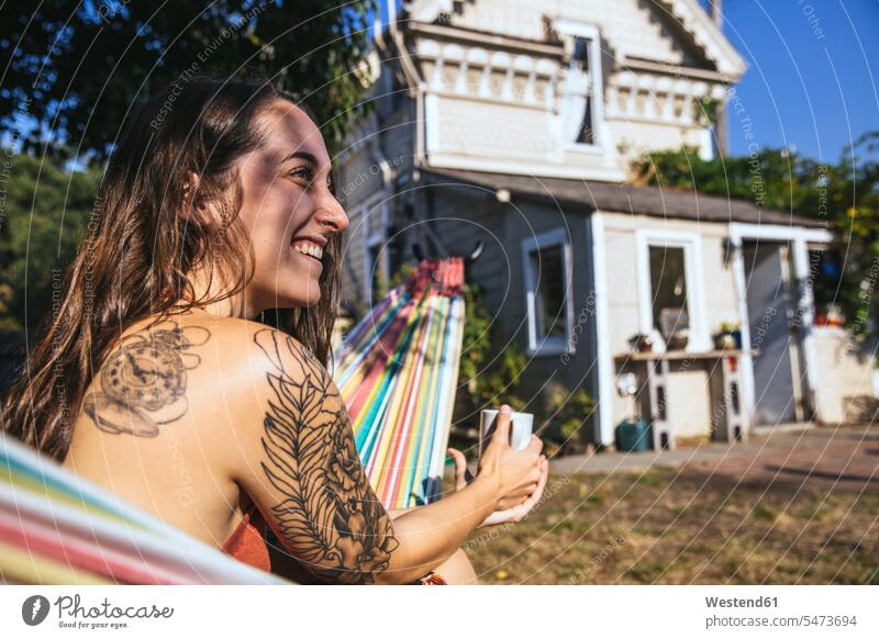 Happy young woman with tattoo in hammock happiness happy females women hammocks tattoos Adults grown-ups grownups adult people persons human being humans