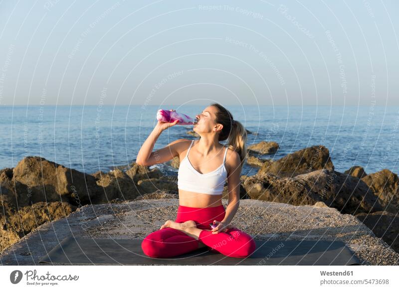 Young woman practicing yoga on the beach, drinking water Seated sit exercise exercising practice practise practising in the morning refreshing skies beaches