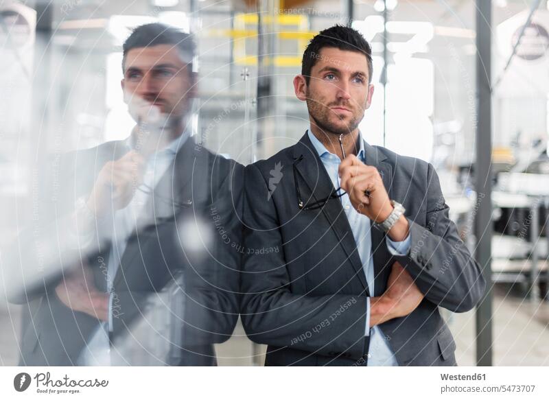 Businessman leaning against glass pane in modern factory thinking glass panes Business man Businessmen Business men contemporary factories business people