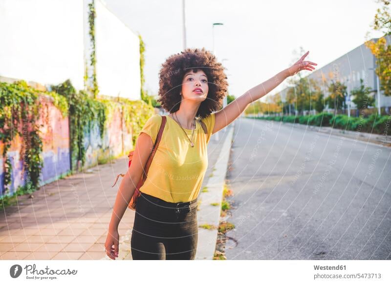 Young woman with afro hairdo hitchhiking in the city human human being human beings humans person persons curl curled curls curly hair back-pack back-packs