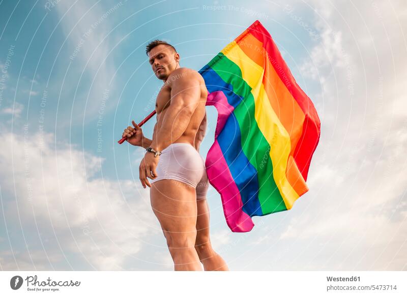 Shirtless young man holding rainbow flag while standing against sky color image colour image Spain leisure activity leisure activities free time leisure time