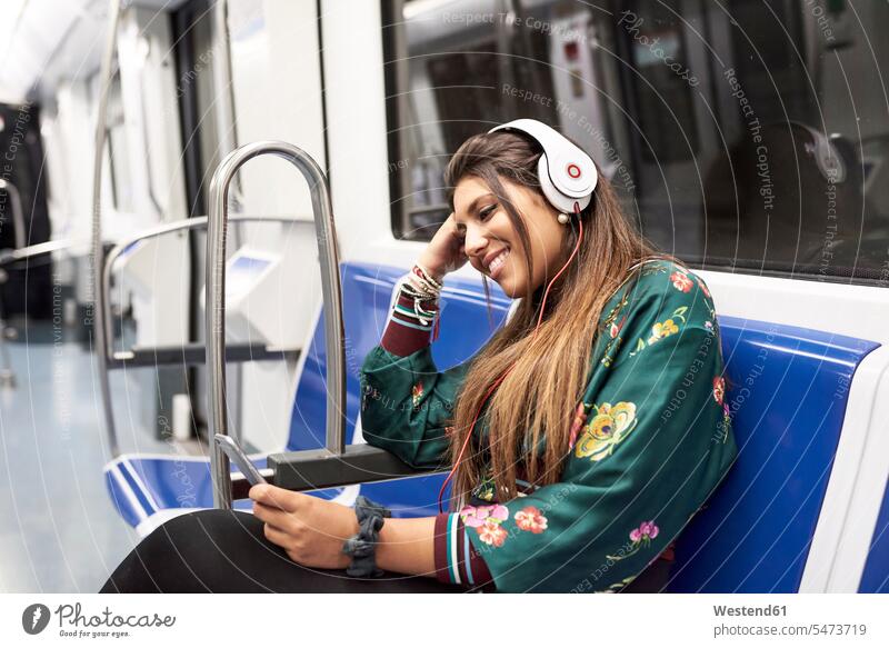 Smiling young woman listening music with headphones and smartphone in underground train smiling smile Smartphone iPhone Smartphones headset hearing females
