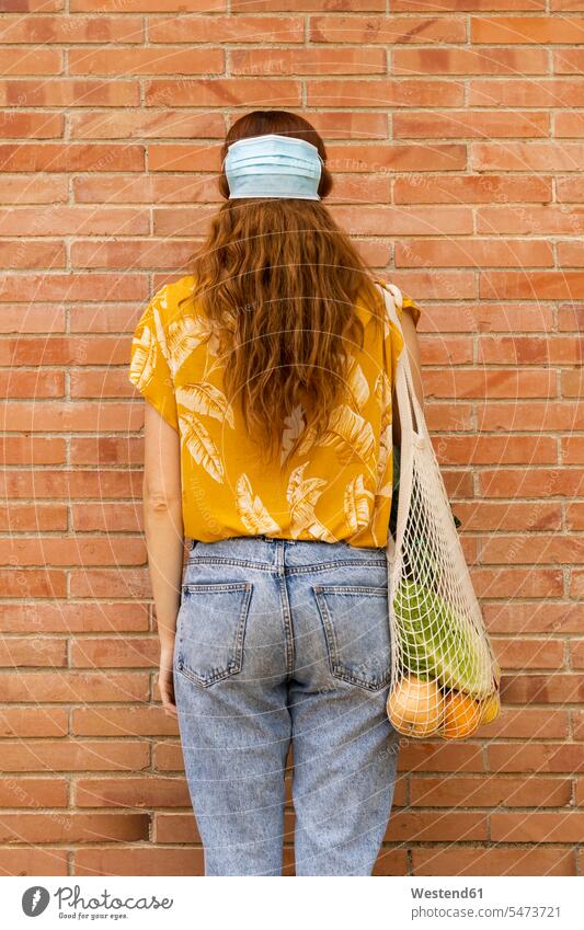 Young woman with grocery shopping bag wearing face mask on hair while standing in front of brick wall color image colour image Spain leisure activity