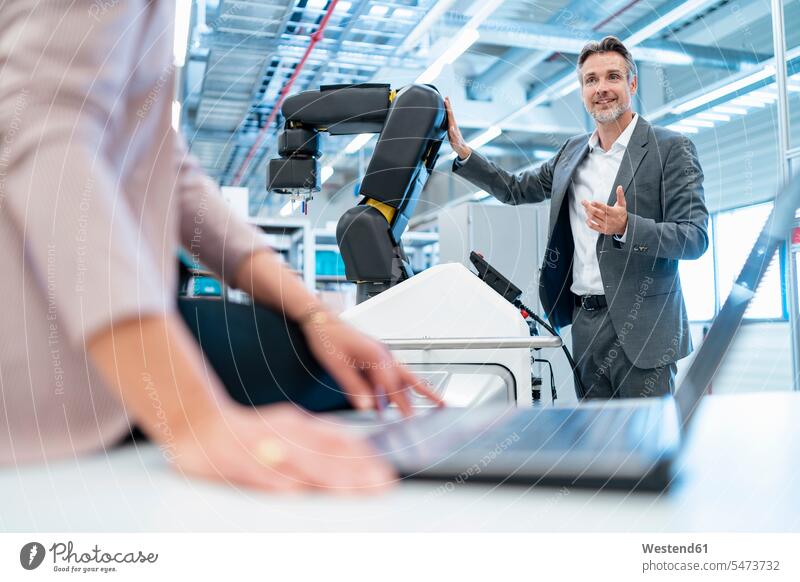 Businessman and businesswoman with laptop and robot in a modern factory hall human human being human beings humans person persons caucasian appearance