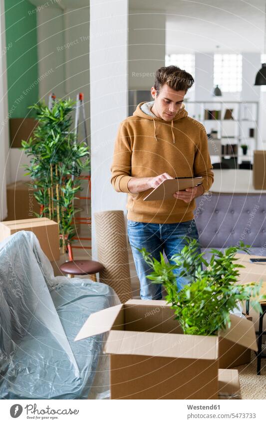 Young man holding list while standing by box with plant in new loft apartment color image colour image indoors indoor shot indoor shots interior interior view