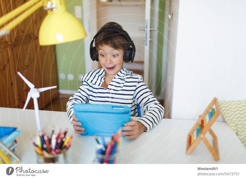 Boy doing homeschooling and using tablet and headphones at home wind turbine wind turbines wind wheels windmill windmills Tables desks headset hear learn play