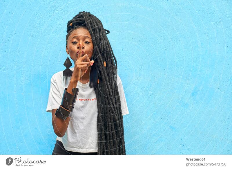 Portrait of woman with long dreadlocks making the silence sign with her finger in front of turquoise wall T- Shirt t-shirts tee-shirt Turquoise Color free time