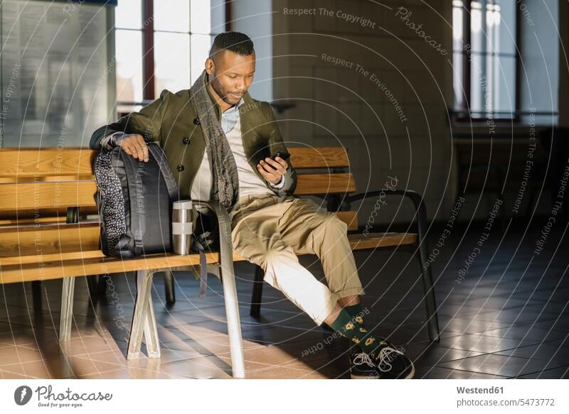 Stylish man using smartphone while sitting on a bench in a train station business life business world business person businesspeople Business man Business men